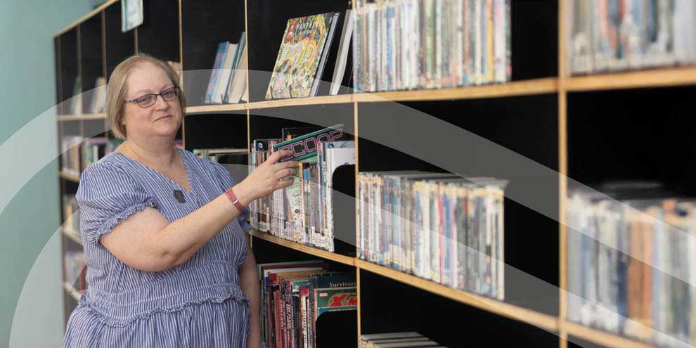 Charly stands by a bookshelf, putting a book away.