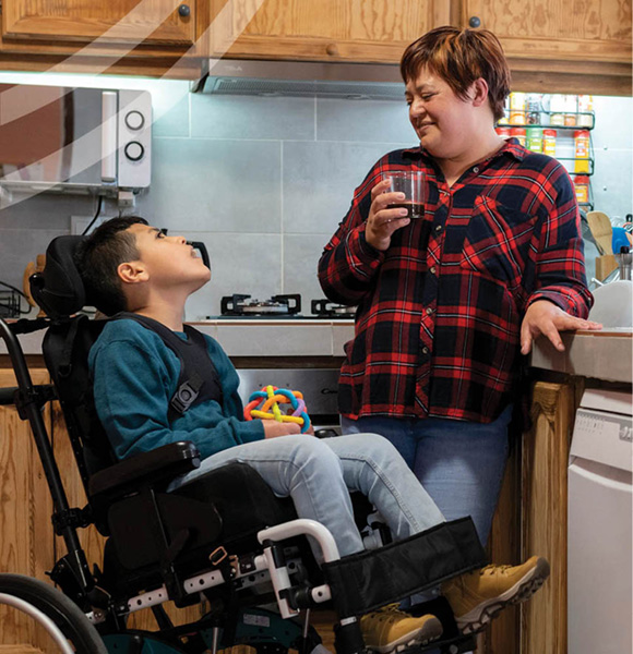 Photo of a person in a wheelchair in a kitchen speaking with someone in plaid shirt