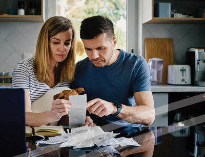 Couple looking stressed while reviewing documents at kitchen table.