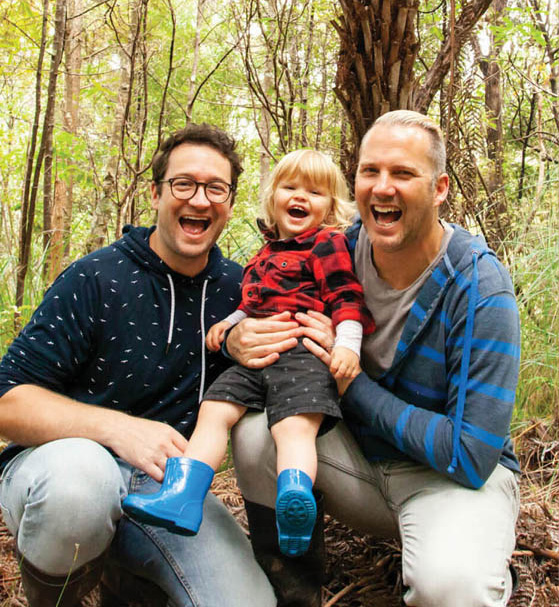 Photo of three people - two adults and a child - smiling together outdoors in nature