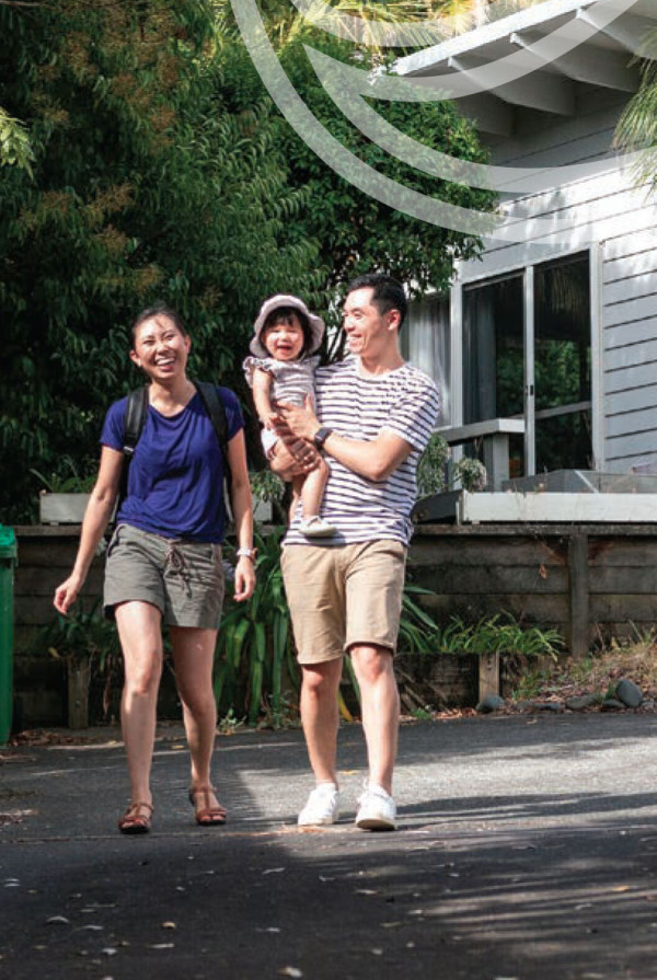 Photo of three people - two adults and a child - standing together outdoors in front of a house