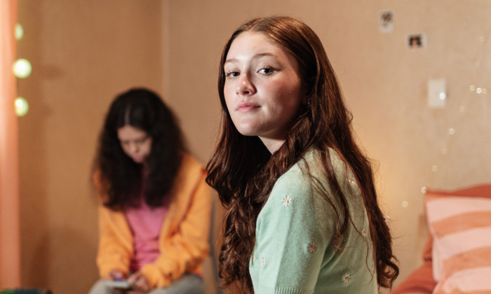 Two teenagers in a bedroom, one looking at the camera with a wistful look.